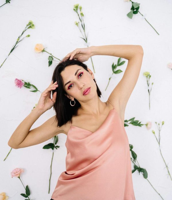 Woman in a graceful yoga pose with soft pink background.